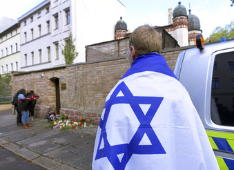 A person with a flag of Israel stands next to flowers and candles in front of a synagogue in Halle, Germany, Thursday, Oct. 10, 2019. A heavily armed assailant ranting about Jews tried to force his way into a synagogue in Germany on Yom Kippur, Judaism's holiest day, then shot two people to death nearby in an attack Wednesday that was livestreamed on a popular gaming site. (AP Photo/Jens Meyer)