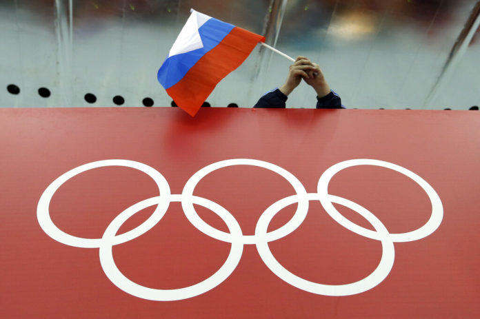 FILE - In this Feb. 18, 2014, file photo, a Russian skating fan holds the country's national flag over the Olympic rings before the start of the men's 10,000-meter speedskating race at Adler Arena Skating Center during the 2014 Winter Olympics in Sochi, Russia. The World Anti-Doping Agency banned Russia on Monday Dec. 9, 2019 from the Olympics and other major sporting events for four years, though many athletes will likely be allowed to compete as neutral athletes. (AP Photo/David J. Phillip, File)