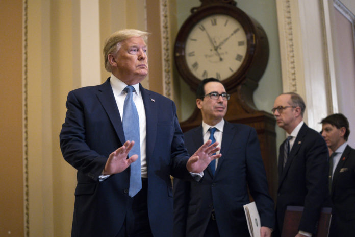 Treasury Secretary Steven Mnuchin listens and President Donald Trump arrives to speak with reporters after meeting with Republican lawmakers on Capitol Hill, Tuesday, March 10, 2020, in Washington. (AP Photo/Evan Vucci)