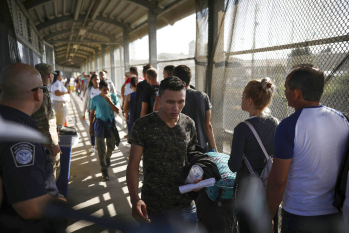 FILE - In this Aug. 2, 2019, file photo, migrants return to Mexico as other migrants line up on their way to request asylum in the U.S., at the foot of the Puerta Mexico bridge in Matamoros, Mexico, that crosses into Brownsville, Texas. One by one, asylum-seekers from El Salvador and Honduras who are waiting in Mexico for court hearings in the United States appeared before an immigration judge to explain why, after months of effort, they couldn't find an attorney. Only 5.3% of asylum-seekers subject to the Migrant Protection Protocols, as the "Remain in Mexico" policy is officially known, had lawyers through the end of January, compared with 85% for asylum-seekers nationwide, according to Syracuse University's Transactional Records Access Clearinghouse. (AP Photo/Emilio Espejel, File)