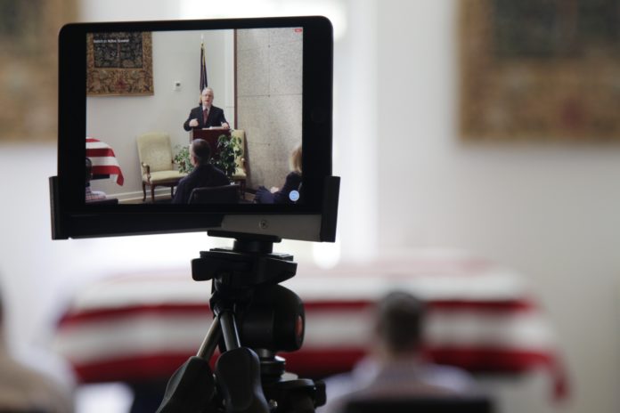 In this Friday, April 3, 2020, photo, a tablet livestreams the funeral of J. Robert Coleman in Lexington, S.C. Following CDC guidelines during the coronavirus outbreak, Thompson Funeral Homes asked Coleman's family to invite fewer than 10 people to his service. (AP Photo/Sarah Blake Morgan)