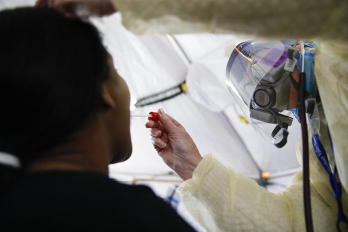 In this April 20, 2020 photo, Catherine Hopkins, Director of Community Outreach and School Health at St. Joseph's Hospital, right, performs a test on a patient in a COVID-19 triage tent at St. Joseph's Hospital in Yonkers, N.Y. New York’s plan for taming the coronavirus hinges on taking a time-tested practice to an extraordinary level: hiring an “army” of people to try to trace everyone who might be infected. It's part of a common approach to controlling infectious diseases -- testing, tracing contacts and isolating those infected. But the scope is staggering even for a public health system that used the technique to combat AIDS and tuberculosis. (AP Photo/John Minchillo)