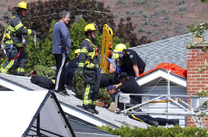 First responders attend to a person on a rooftop at the scene of a crash involving a Canadian Forces Snowbirds airplane in Kamloops, British Columbia, Sunday, May 17, 2020. (Brendan Kergin/Castanet Kamloops/The Canadian Press via AP)