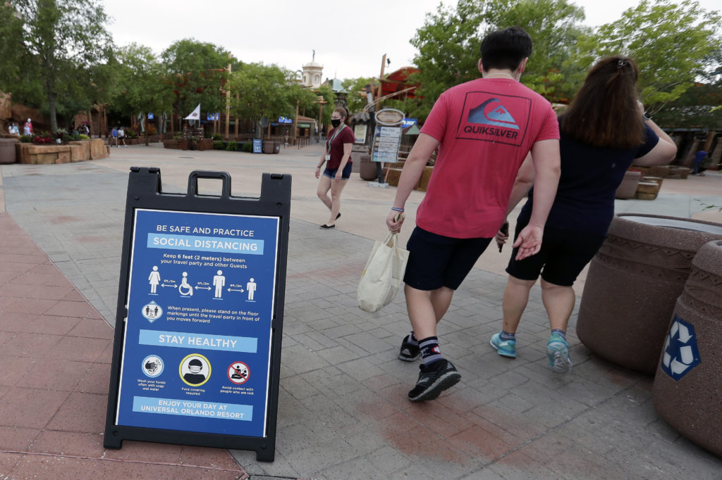 In this Wednesday, June 3, 2020 photo, signs about social distancing and other protocols are seen about the theme park as guests walk by at Universal Orlando Resort Wednesday, June 3, 2020, in Orlando, Fla. The theme park has reopened for season pass holders and will open to the general public on Friday, June 5. (AP Photo/John Raoux)