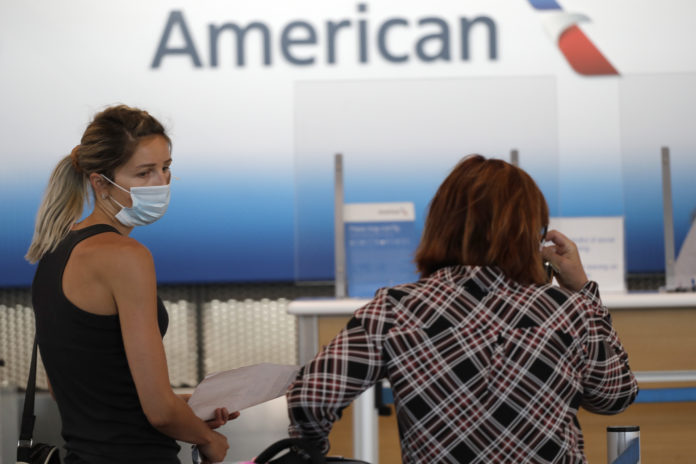 In this June 16, 2020 file photo travelers wear masks as they wait at the American Airlines ticket counter at O'Hare International Airport in Chicago. American Airlines has banned a man who was kicked off a plane for refusing to wear a face covering, among the first such incidents since airlines promised this week to step up enforcement of their mask rules. A spokesman for American said Thursday, June 18, 2020 that the airline decided to ban the man after reviewing the incident, which occurred Wednesday at New York's LaGuardia Airport. (AP Photo/Nam Y. Huh)