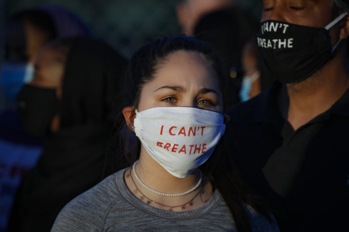 Madeline Curry attends a protest with her father outside the Minneapolis 5th Police Precinct while wearing a protective mask that reads "I CAN'T BREATHE", Saturday, May 30, 2020, in Minneapolis. Protests continued following the death of George Floyd, who died after being restrained by Minneapolis police officers on Memorial Day. (AP Photo/John Minchillo)