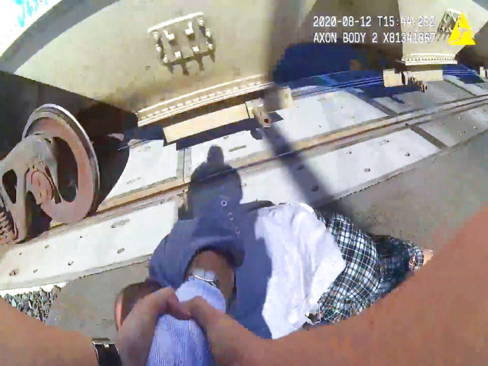 This photo from body camera video carried by Lodi, Calif., Police Officer Erika Urrea as she pulls a man from the path of a passing train on Wednesday, Aug. 13, 2020. The man in a wheelchair was stuck on railroad tracks seconds before the train came past, in a dramatic rescue caught on the officer's body camera. The Lodi Police Department says Urrea was patrolling Wednesday near the tracks when she saw the man and the railroad crossing arms starting to come down. Unable to move the wheelchair, Urrea is seen dragging the man from it seconds before the train barrels through, striking the wheelchair and the man's leg. The 66-year-old man is at a hospital in stable condition. ( Lodi Police Department via AP)