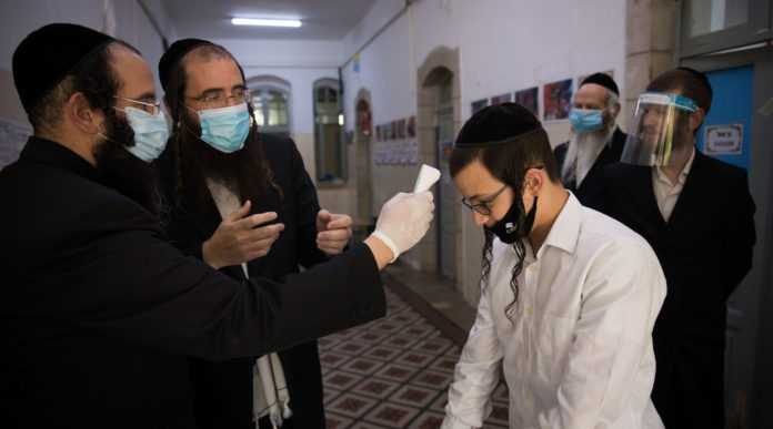 A teacher checks the temperature of a student to identify if he have fever at the entrance to at an Ultra-Orthodox school founded by Rabbi Shmuel Stern in Jerusalem on May 6, 2020. Photo by Nati Shohat/Flash90