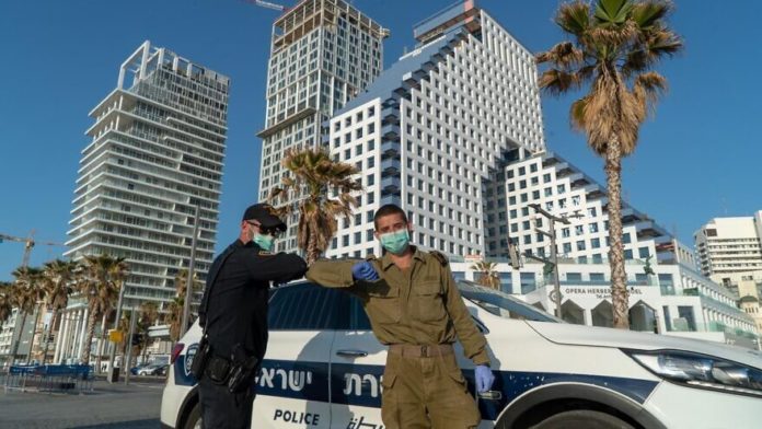A IDF soldier and Israel Police do an elbow bump in front of one of the IDF Homefront Command''s coronavirus hotels in Tel Aviv. Credit: IDF Spokesperson's Unit.