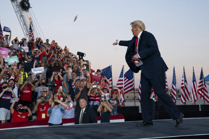 President Donald Trump throws face masks into the crowd as he arrives for a campaign rally at Orlando Sanford International Airport, Monday, Oct. 12, 2020, in Sanford, Fla. (AP Photo/Evan Vucci)