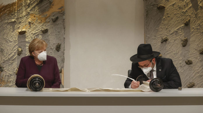 German Chancellor Angela Merkel watches Rabbi Shaul Nekrich complete the historic Sulzbach Torah Scroll in Berlin, Jan. 27, 2021. (Odd Andersen/Pool/Getty Images)