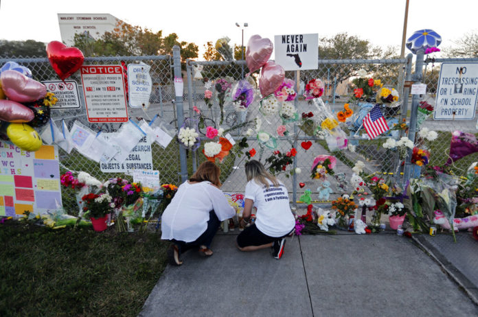 FILE - In this Feb. 18, 2018 file photo, people light candles at a makeshift memorial outside Marjory Stoneman Douglas High School, where 17 students and faculty were killed in a mass shooting days earlier in Parkland, Fla. Sorrow is reverberating across the country Sunday, Feb. 14, 2021, as Americans joined a Florida community in remembering the 17 lives lost three years ago in the Parkland school shooting massacre. President Joe Biden used the the occasion to call on Congress to strengthen gun laws, including requiring background checks on all gun sales and banning assault weapons. (AP Photo/Gerald Herbert, File)
