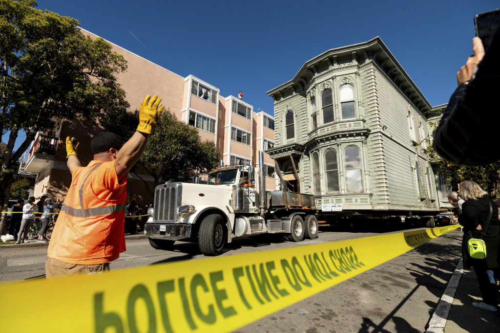 A worker signals to a truck driver pulling a Victorian home through San Francisco on Sunday, Feb. 21, 2021. The house, built in 1882, was moved to a new location about six blocks away to make room for a condominium development. According to the consultant overseeing the project, the move cost approximately $200,000 and involved removing street lights, parking meters, and utility lines. (AP Photo/Noah Berger)