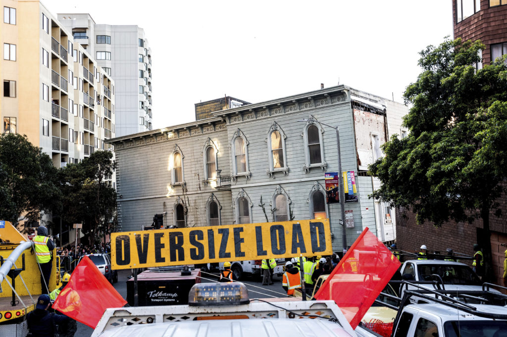 A truck pulls a Victorian home through San Francisco on Sunday, Feb. 21, 2021. The house, built in 1882, was moved to a new location about six blocks away to make room for a condominium development. According to the consultant overseeing the project, the move cost approximately $200,000 and involved removing street lights, parking meters, and utility lines. (AP Photo/Noah Berger)